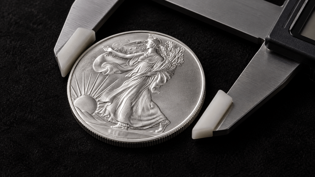 Padded caliper jaws positioned around the edge of a silver-colored coin.